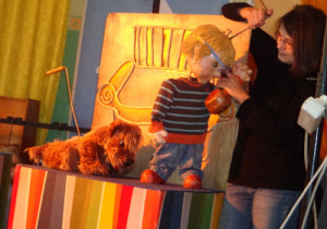 Animatorka trzyma marionetkę chłopca, a obok niego stoi marionetka psa.
